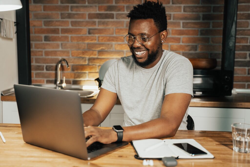 A smiling man seated at a desk working on his laptop: outsourced research