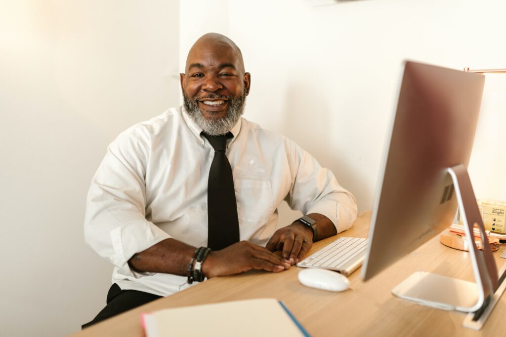 A smiling man in a shirt and tie sitting at a desk: outsourced receptionist